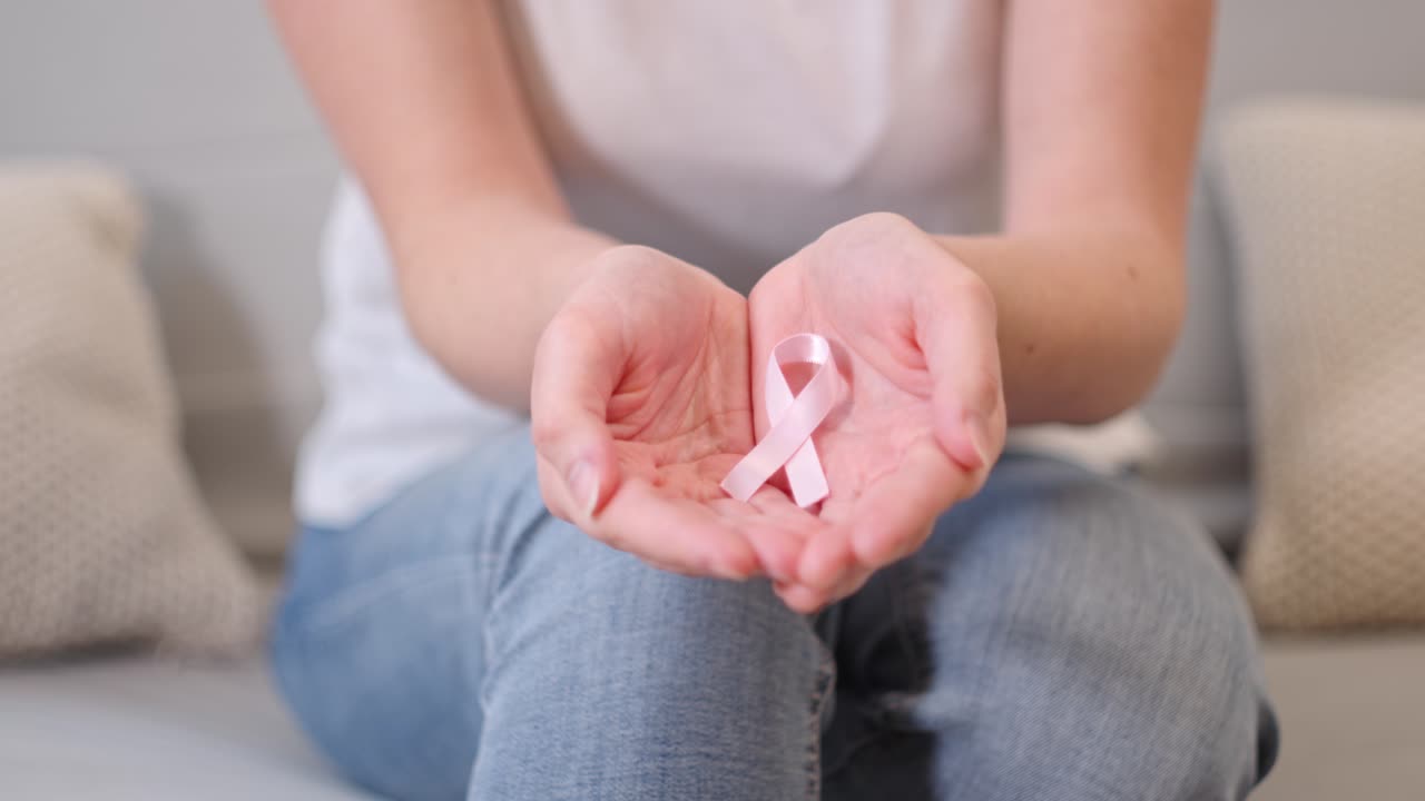 una mujer sentada en el sofá muestra su palma con una cinta rosa.