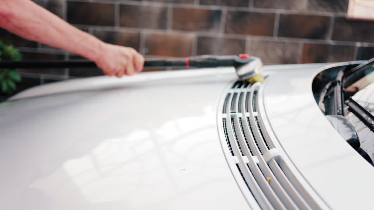 Close up of a car hood being scrubbed with a brush and water