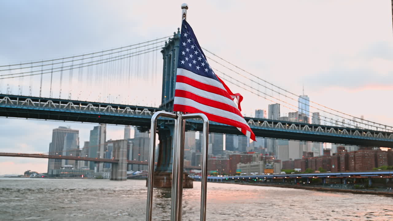 Eine im Wind wehende amerikanische Flagge, die an das Metallgeländer angepasst ist. Blickwinkel von unten auf die Manhattan Bridge im Hintergrund.