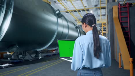 back view of asian woman using laptop computer with mock up green screen in pipe manufacturing factory