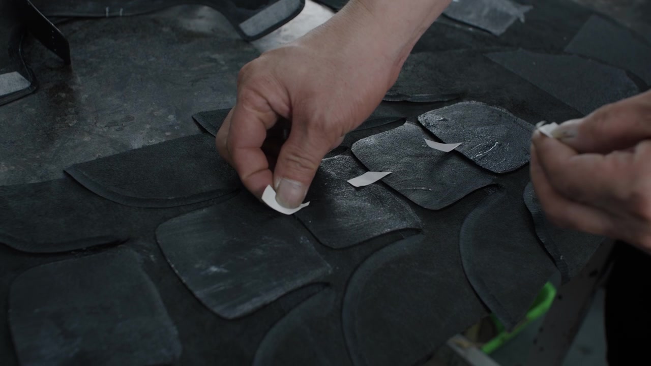 Worker applies adhesive strips to black shoe components on a factory worktable