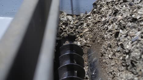 closeup of automated auger loading processed wood chip into a biomass boiler