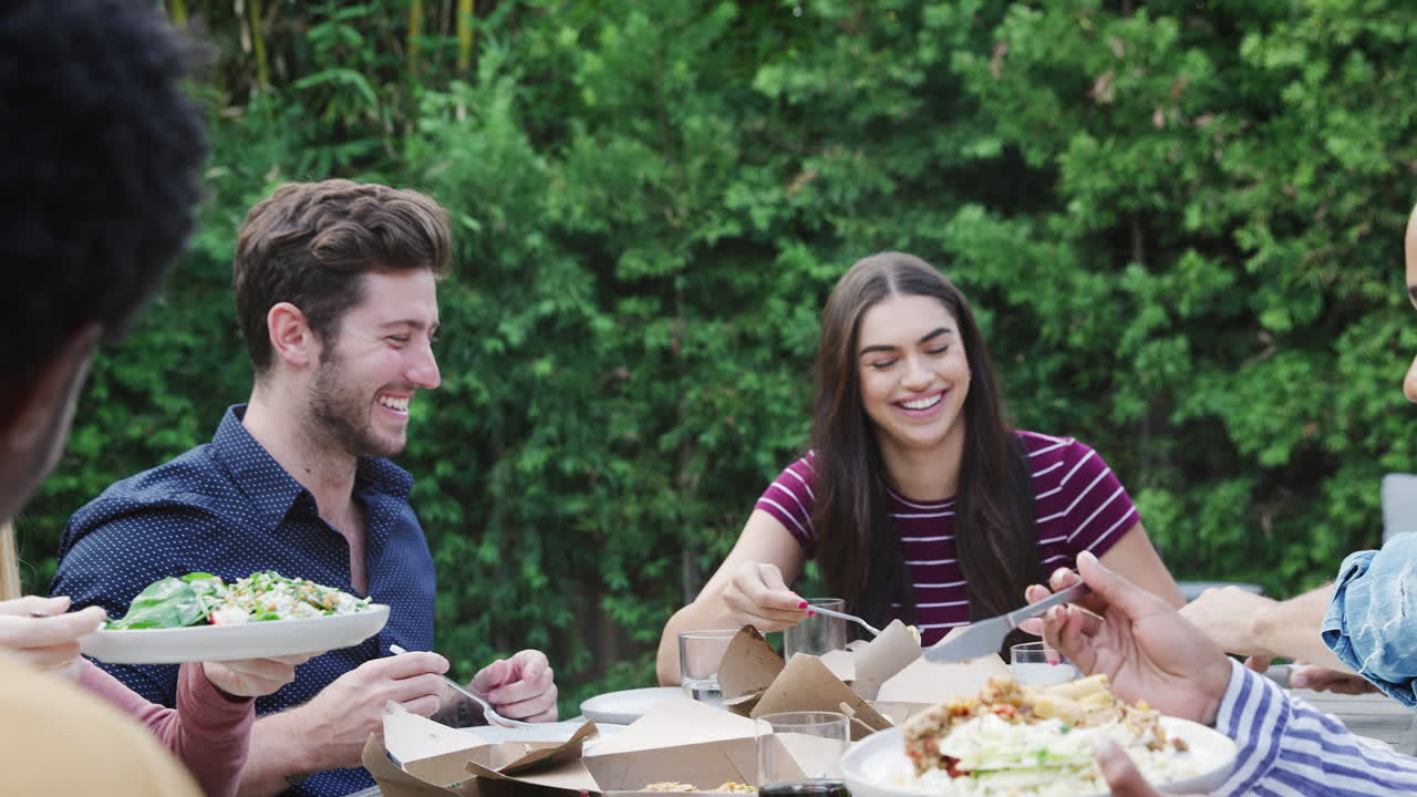 amigos multiculturales en casa sentados a la mesa disfrutando de la comida en la fiesta del jardín de verano