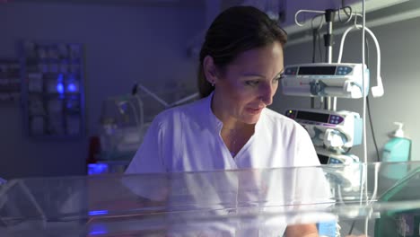 enfermera tocando suavemente al frágil recién nacido en la incubadora neonatal
