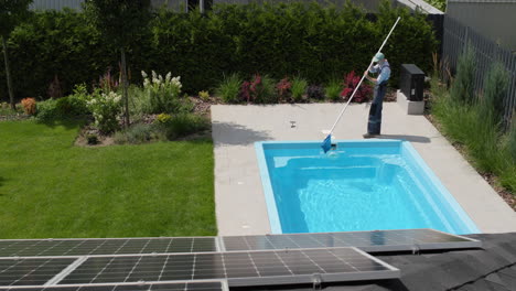 un trabajador quita los escombros de una piscina con una red.