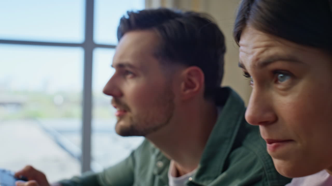 People hands pressing consoles buttons at couch closeup. Guy girl competition