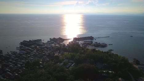 aerial flight towards local village and ocean with golden sky in background in malaysia, extreme long shot moving forward in slow motion