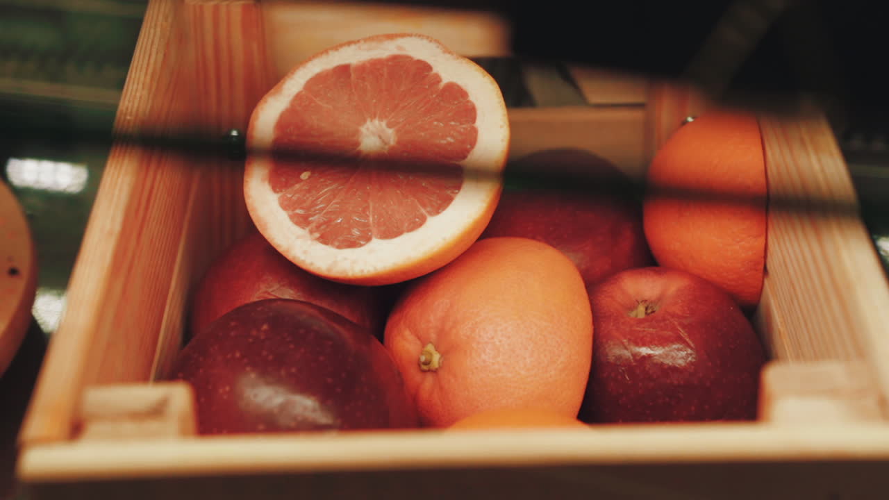 Fresh grapefruit, citrus fruits and apples in a wooden crate. Grapefruit cut in half in a fruit basket. Close up, dolly left. Warm colors.