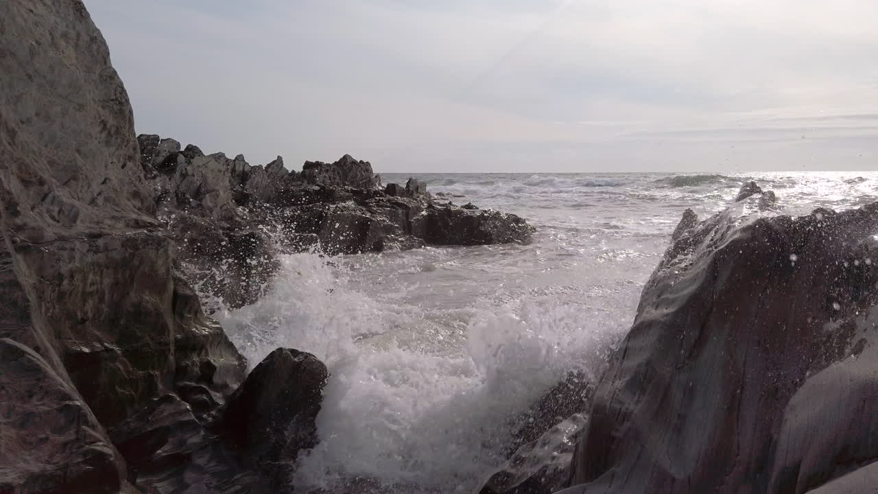 olas rompiendo en una brecha estrecha en una playa rocosa al atardecer