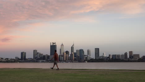 man going for early morning walk, river and city skyline in background, fixed wide shot