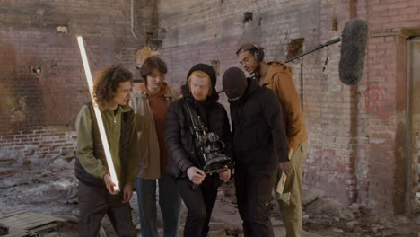 production team, cameraman and actors reviewing a scene movie in a camera in a ruined building