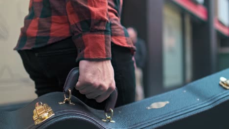 Up-close-shot-of-a-guitar-case-being-held-by-a-musician