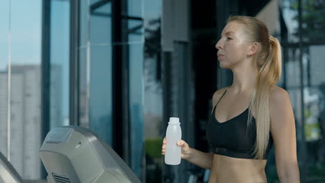 woman hydrating after workout on treadmill at gym
