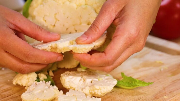hände, die blumenkohl in kleinere stücke brechen