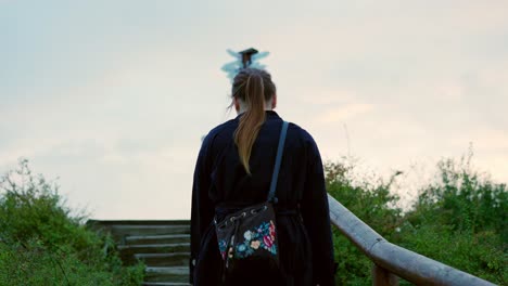 Girl-in-a-long-black-coat-with-her-hair-in-a-ponytail-is-walking-on-the-stairs-in-a-nature-park-in-autumn