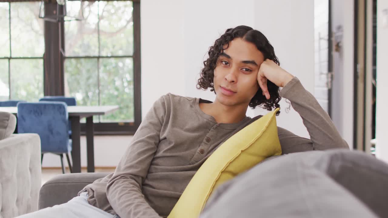 Portrett av lykkelig birasial mann som sitter i sofaen, ser inn i kameraet og smiler