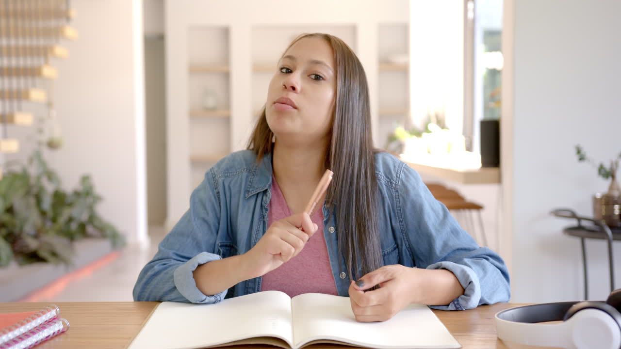 Teen girl studying at home, holding pen and looking at camera