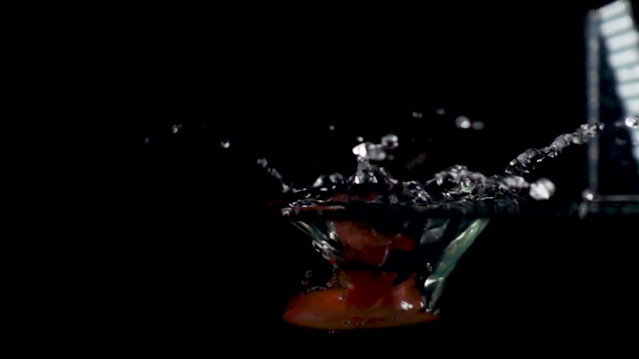 cámara de alta velocidad movimiento lento video inverso de una rodaja de tomate rojo salpicando en el agua