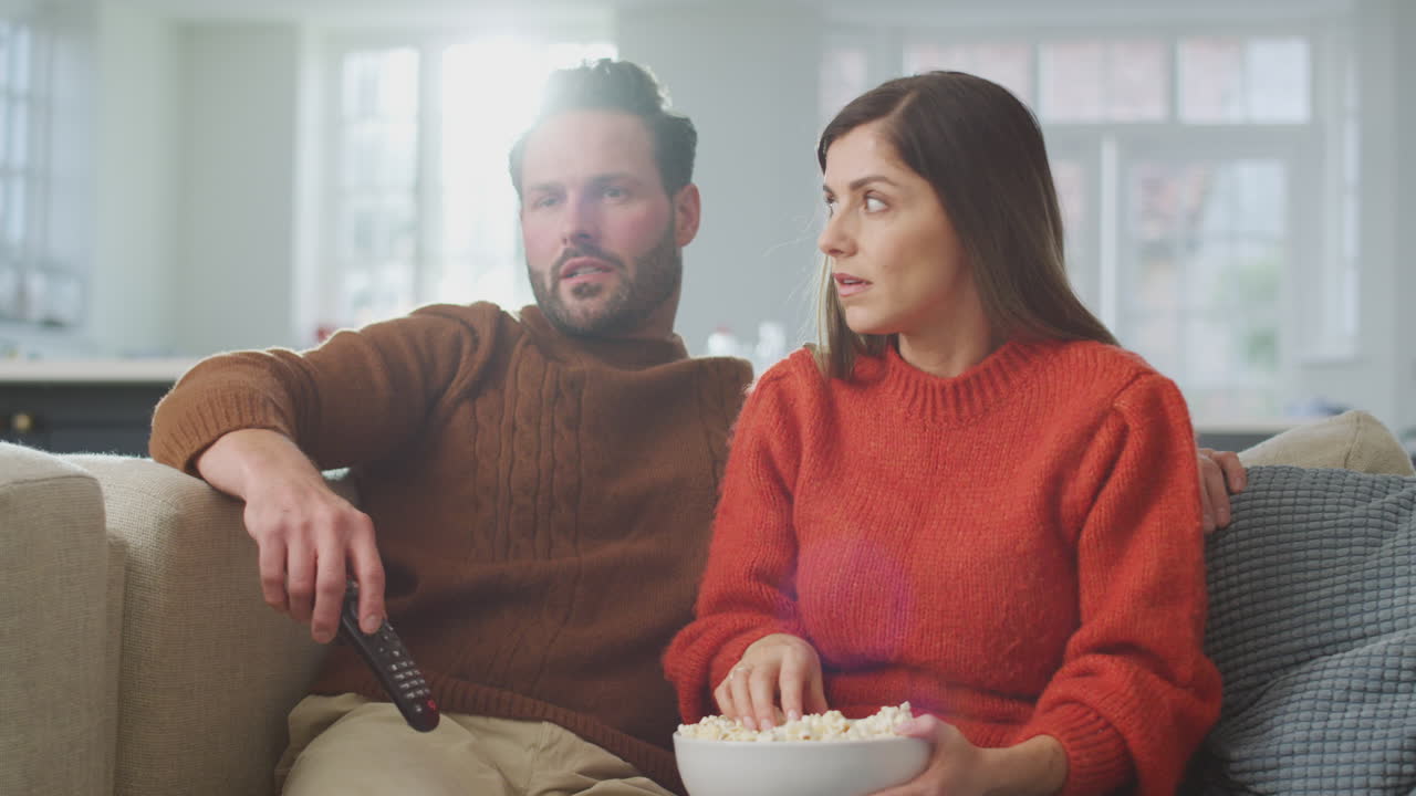 Pareja sentada en el sofá derramando palomitas mientras ven un thriller juntos en la televisión