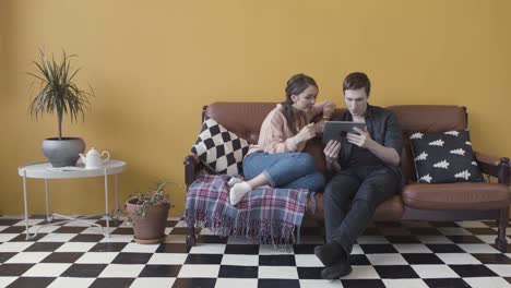 couple relaxing on sofa and watching tablet