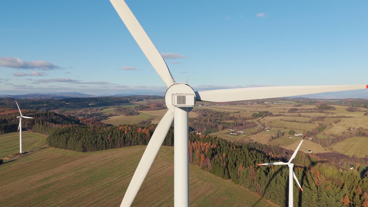 Close drone view of rotating windmill blades over a peaceful rural landscape