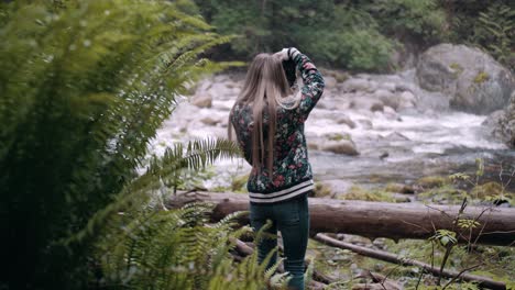 orbit shot revealing a pretty wowan taking photos of a river in lynn valley, vancouver