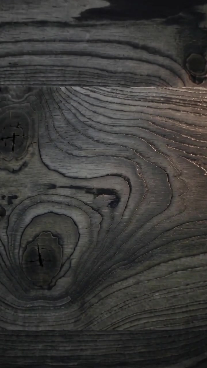 Video vertical: Cámara moviéndose hacia adentro sobre una tabla de madera mientras un destello se desliza, mostrando la veta y los nudos en una habitación.