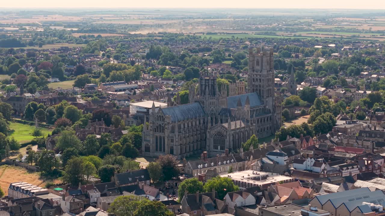Aerial drone partially orbits Ely Cathedral, starting at the side and moving gently left at constant height. Highlights the medieval towers and historic architecture of this iconic English landmark