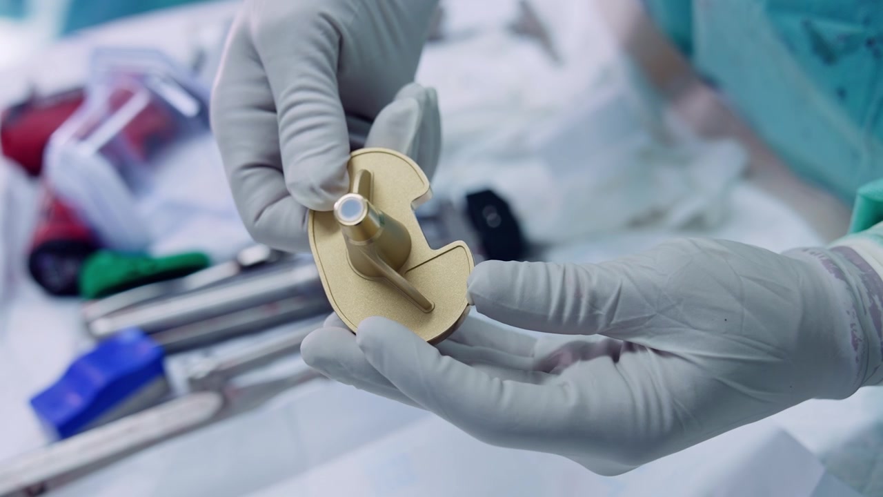 Gloved hands of doctor showing the detail for knee prosthesis. Medic puts down the piece on the surgical stand. Close up.