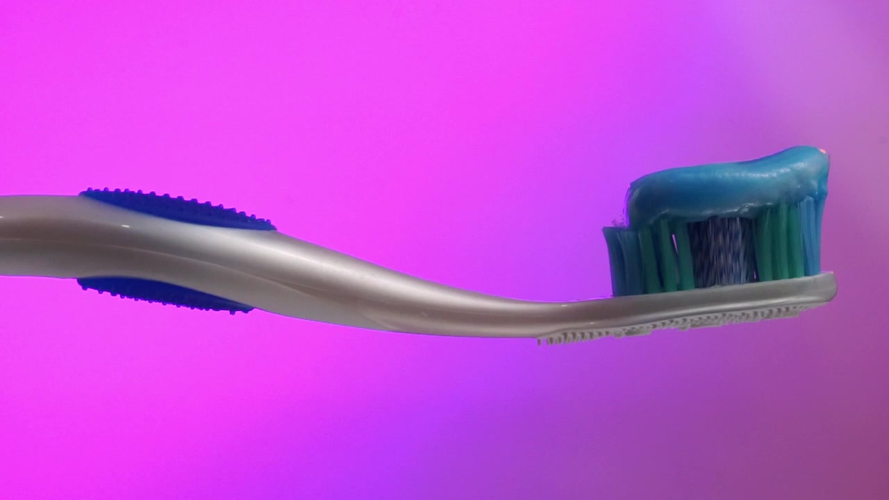 Toothbrush with blue toothpaste against pink background, highlighting dental care