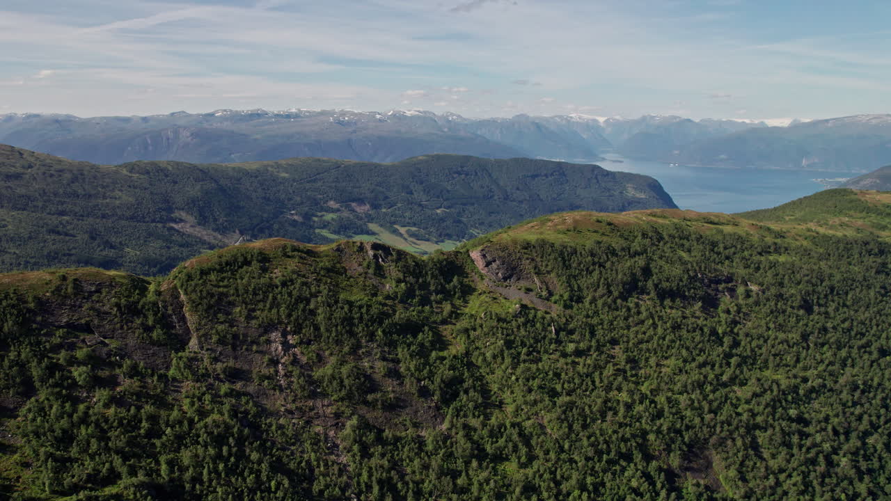 fotografía aérea, que se eleva sobre una cresta bordeada de árboles, revelando montañas cubiertas de nieve y un fiordo