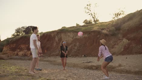 jóvenes amigos alegres jugando al voleibol en la playa junto al mar durante la puesta de sol.