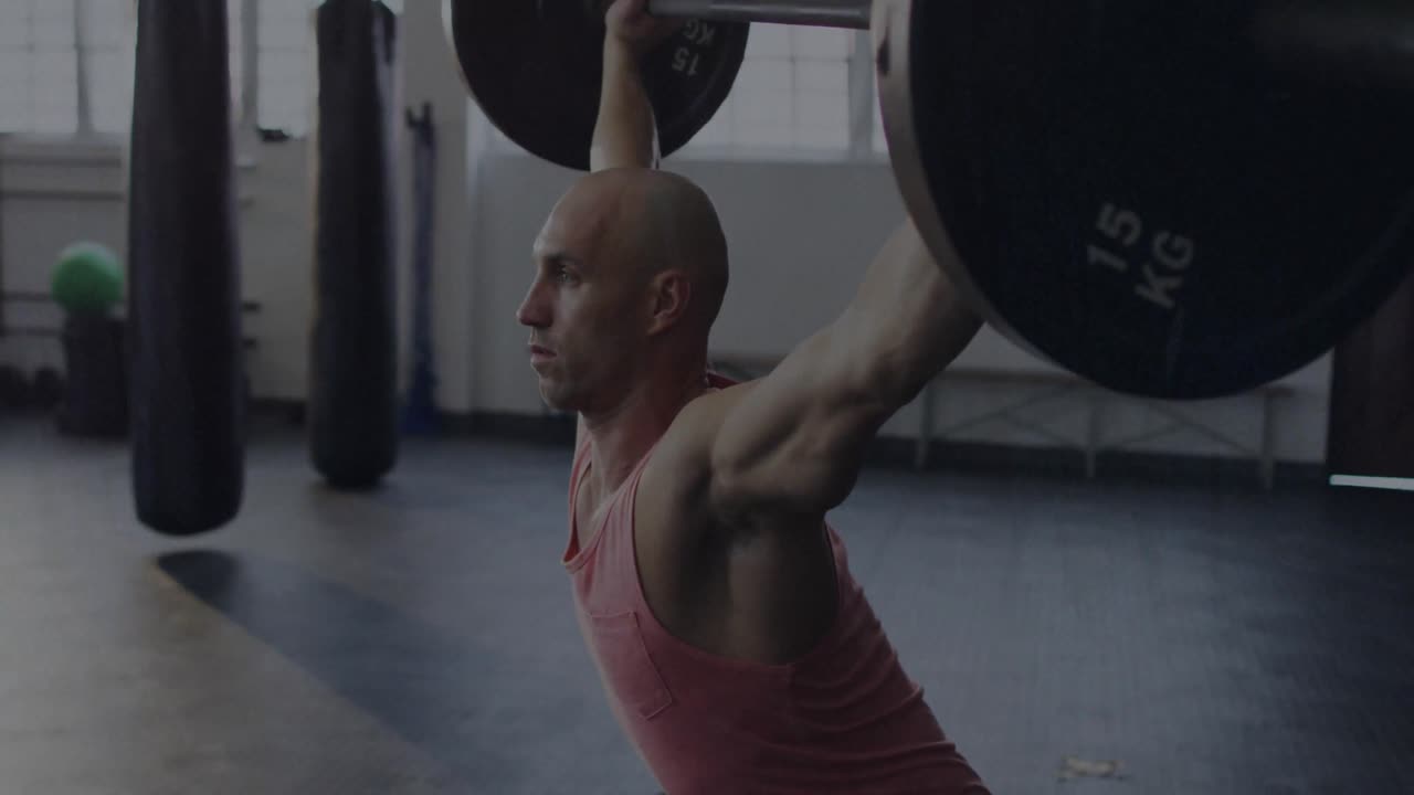 Male gymgoer gripping barbell executing overhead squat in gym while static overlay flickering