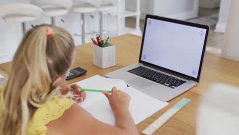 Happy-caucasian-girl-at-home,-writing-during-online-school-lesson-using-laptop,-copy-space-on-screen