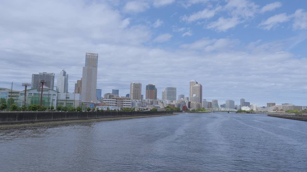 A wide, peaceful shot of the Tokyo skyline with tall skyscrapers and modern buildings along the river on a clear day
