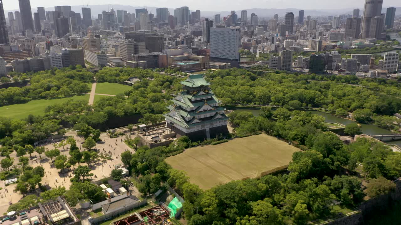 Aerial rising over historic landmark Osaka Castle with park, moat, skyscraper, and city in Osaka, Japan