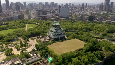 Aerial-rising-over-historic-landmark-Osaka-Castle-with-park,-moat,-skyscraper,-and-city-in-Osaka,-Japan