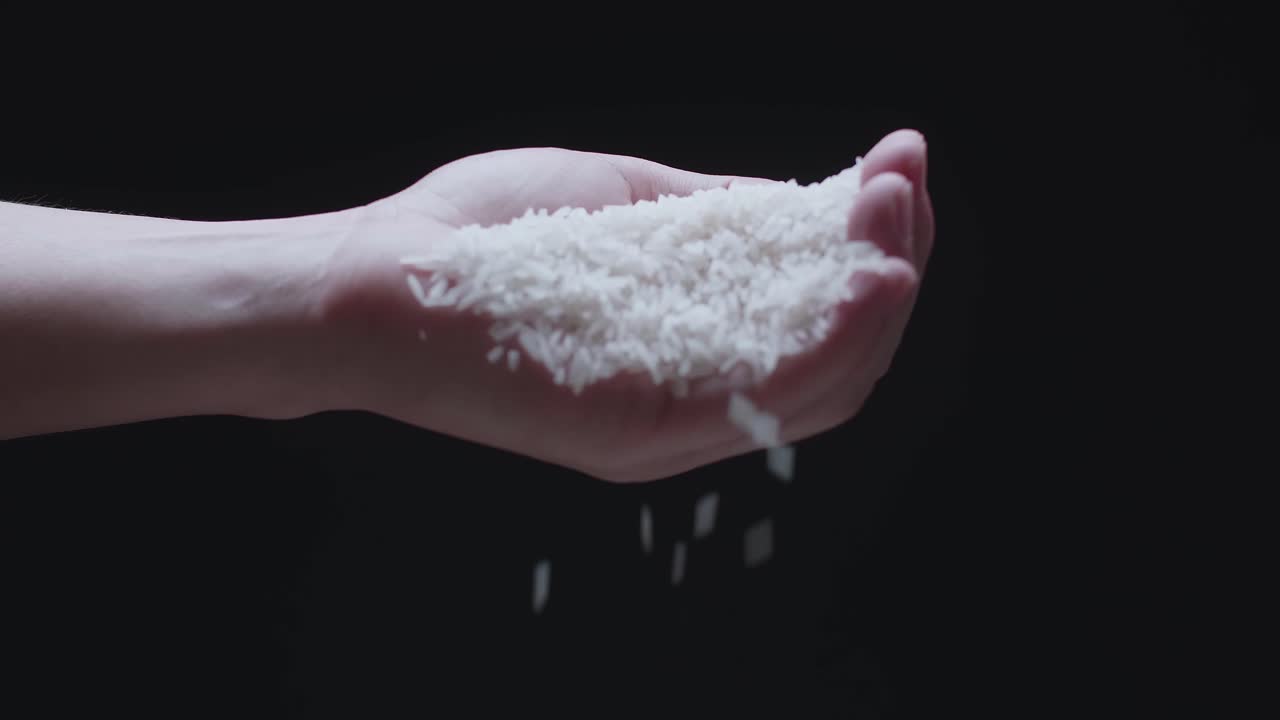 Rice Grains Falling From Hand In Slow Motion  Over A Dark Background