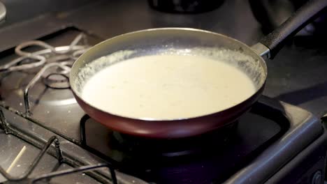 primer plano de una sartén en una estufa con leche cremosa hirviendo suavemente. una mano agrega queso mozzarella picado a la mezcla, derritiéndose en la crema para crear una base rica y quesada
