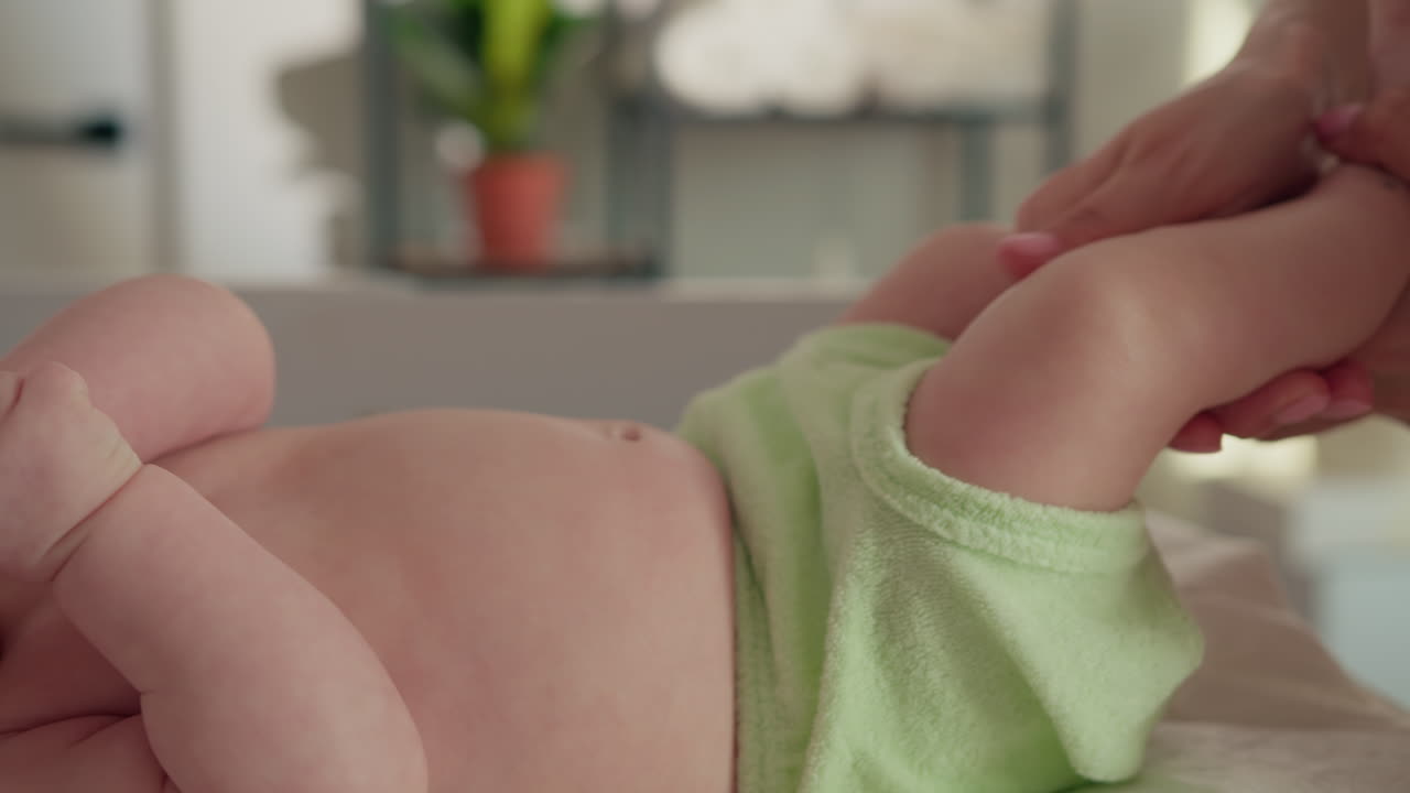 Mani genitoriali che massaggiano delicatamente le gambe e il corpo di un neonato, promuovendo relax e legame in un ambiente calmo.