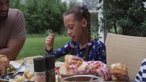 happy biracial father, son and daughter eating meal at dinner table in garden, slow motion