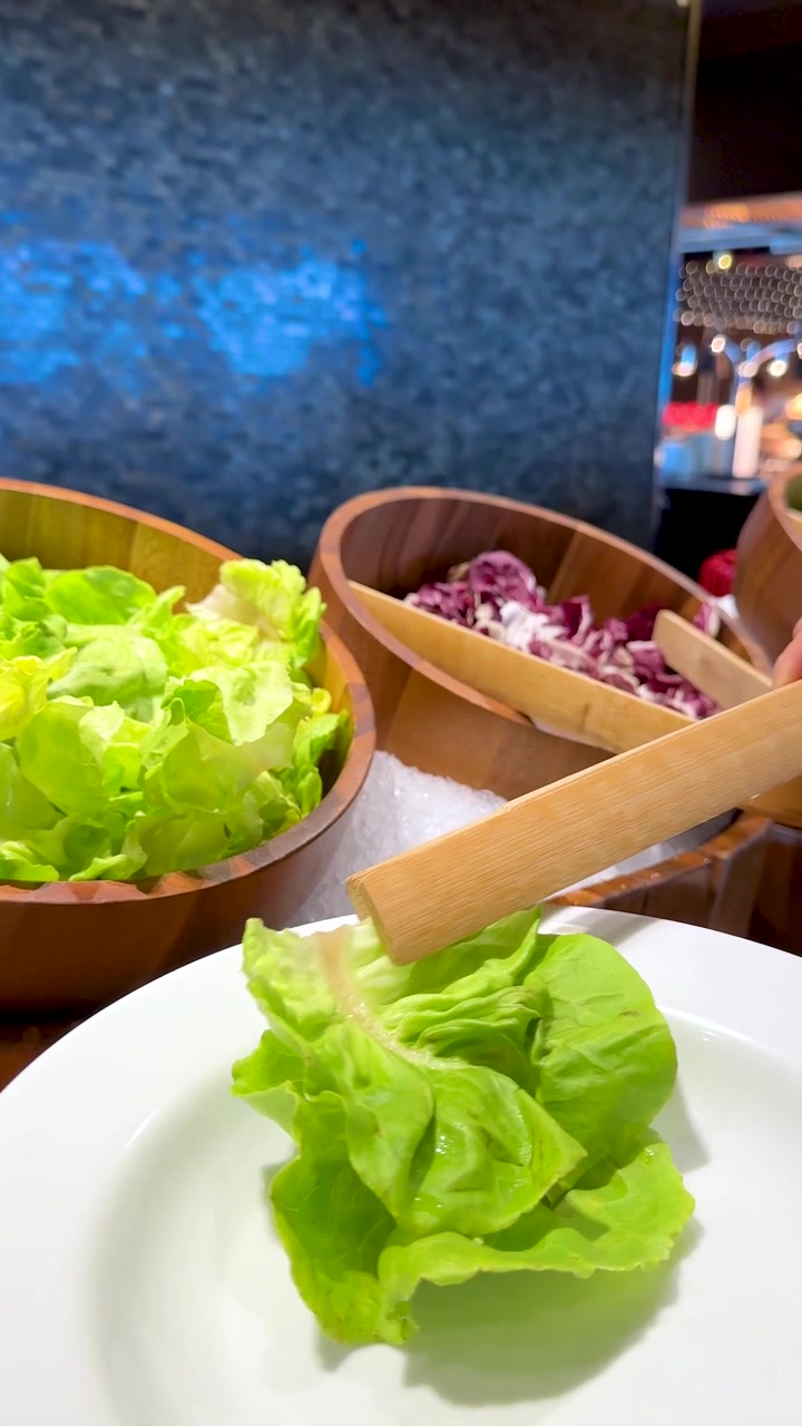 En person bruger trætænger til at tage frisk grøn salat fra en buffetskål.