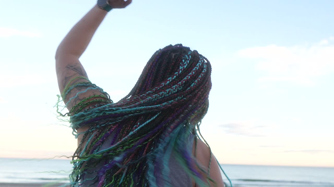 mujer con trenzas coloridas bailando con libertad en la playa