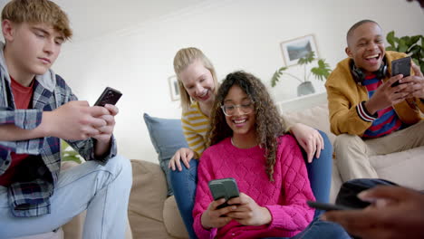 happy diverse group of teenage friends using smartphones and laughing at home, slow motion