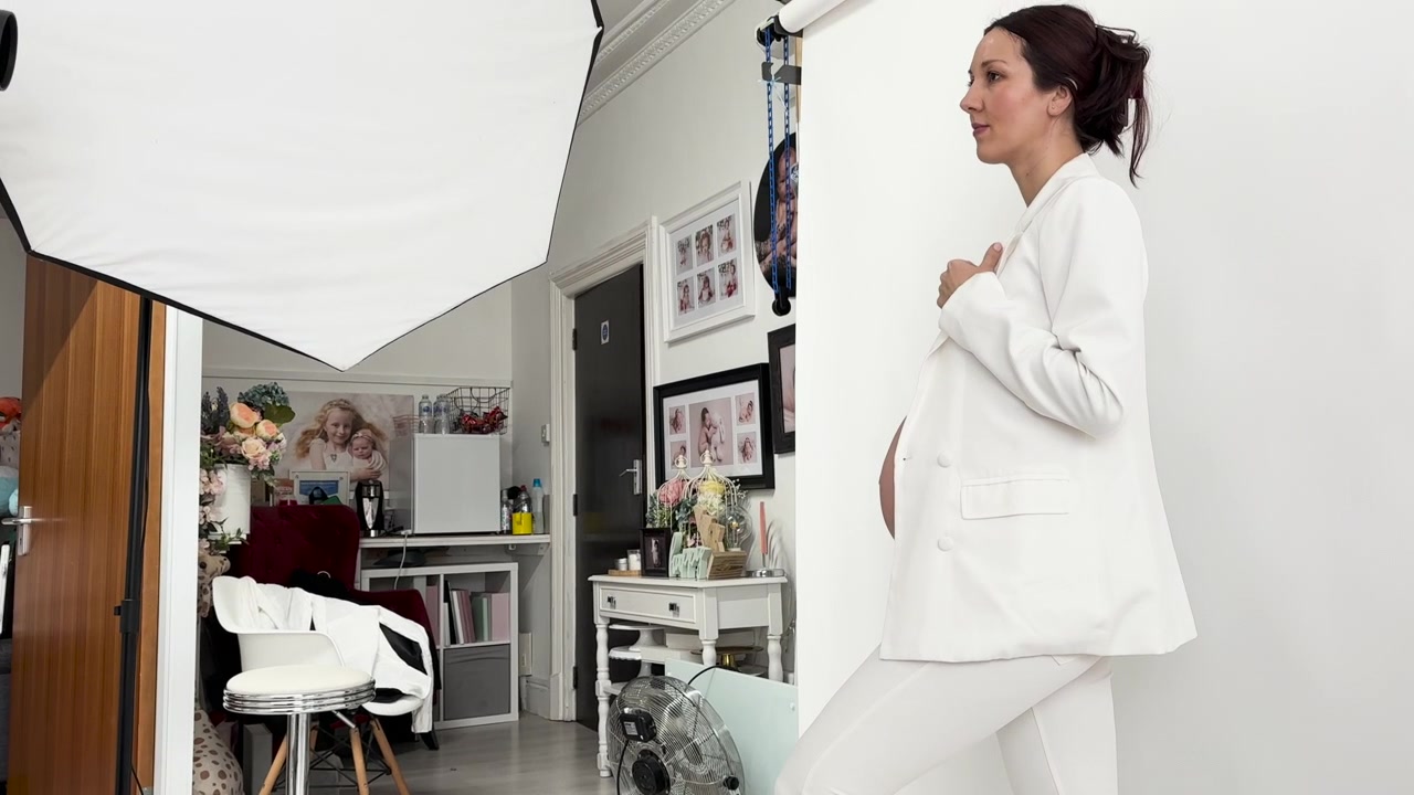 Una mujer con un traje coordinado blanco posa para una sesión de fotos de maternidad - Toma con paneo ascendente