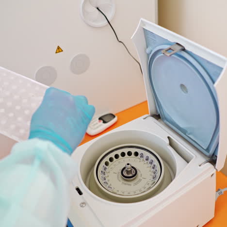 modern apparatus for checking samples in lab. hand in blue glove puts plastic tubes with blood tests to orifices of centrifuge.
