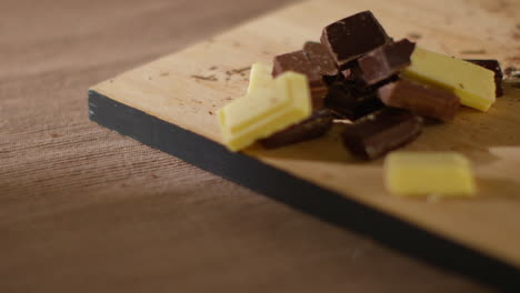 close up of person putting chunks of milk plain and white chocolate onto chopping board