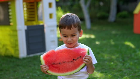 adorable smiling caucasian baby boy holding a big slice of watermelon. happy child eating fruit outdoors.
