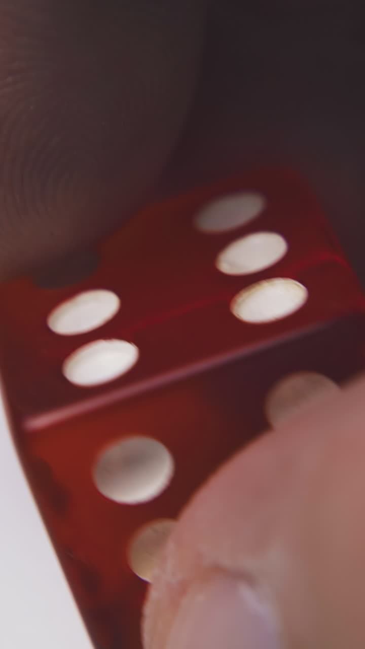 person holds bright red plastic dice with symbol six of spots on sides in white background extreme close view