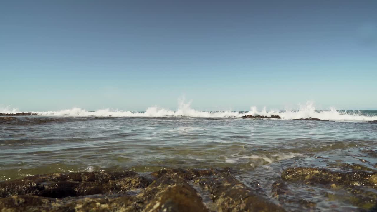 장벽 암초와 조수 웅덩이를 만드는 용암 암석 위로 작은 파도가 굴러갑니다.